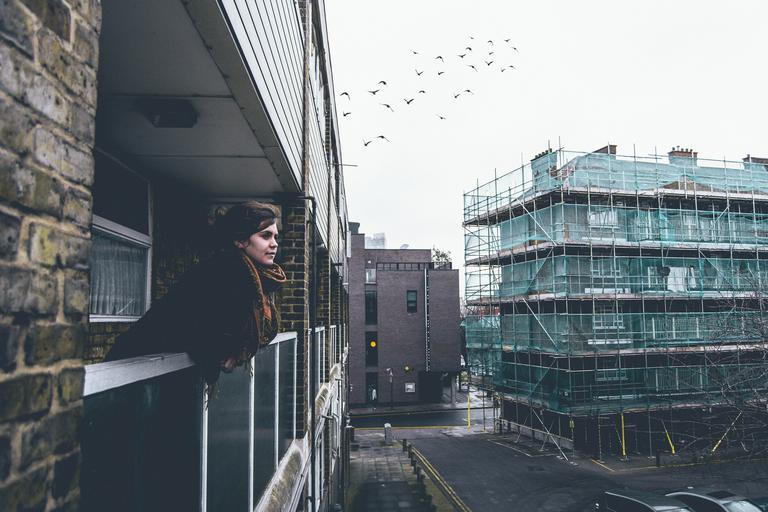 Žena stojí na balkóne opretá o sklenené zábradlie.jpg